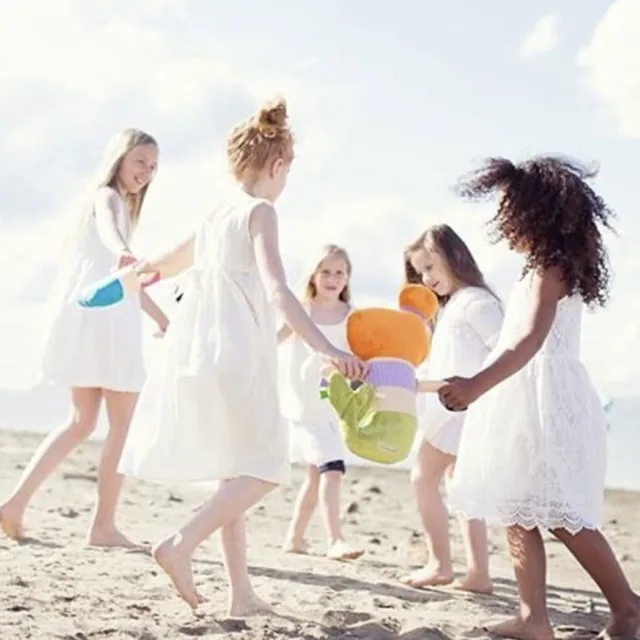 Des fillettes en robes blanches dansent en ronde sur la plage avec la peluche sirène des TrOnches.